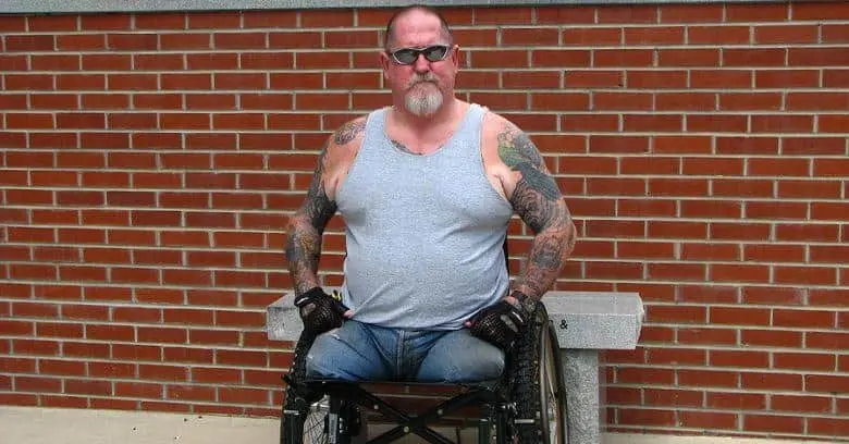 Veteran in wheelchair outside brick wall Veteran in wheelchair with tattoos standing against brick wall.