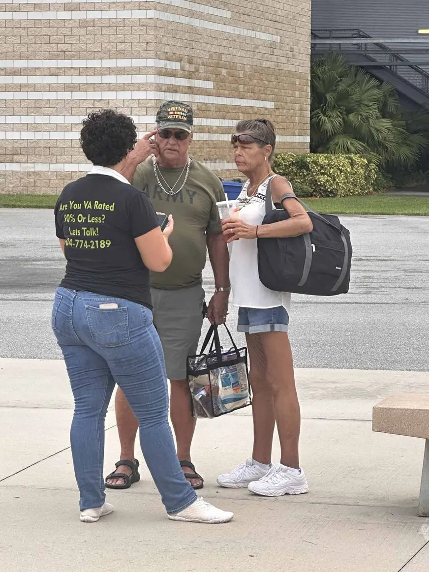Group of three people talking outside near a brick building.