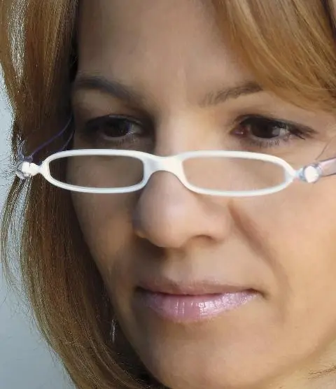 Woman wearing reading glasses with narrow lenses and smiling.