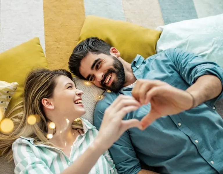 Happy Couple Enjoying a Secure Future with Term Life Insurance Happy young couple lying on pillows, smiling and making a heart shape with their hands, symbolizing love, security, and a protected future.