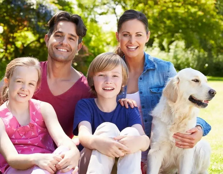 Happy family with two children and a golden retriever sitting outdoors, smiling together, representing financial security and peace of mind with term life insurance.