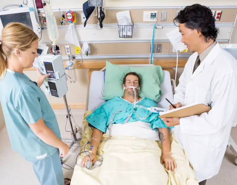 A patient in a hospital bed receiving intensive care, with a doctor and nurse providing medical attention. Represents critical illness coverage through supplemental health insurance in Plano, Texas.