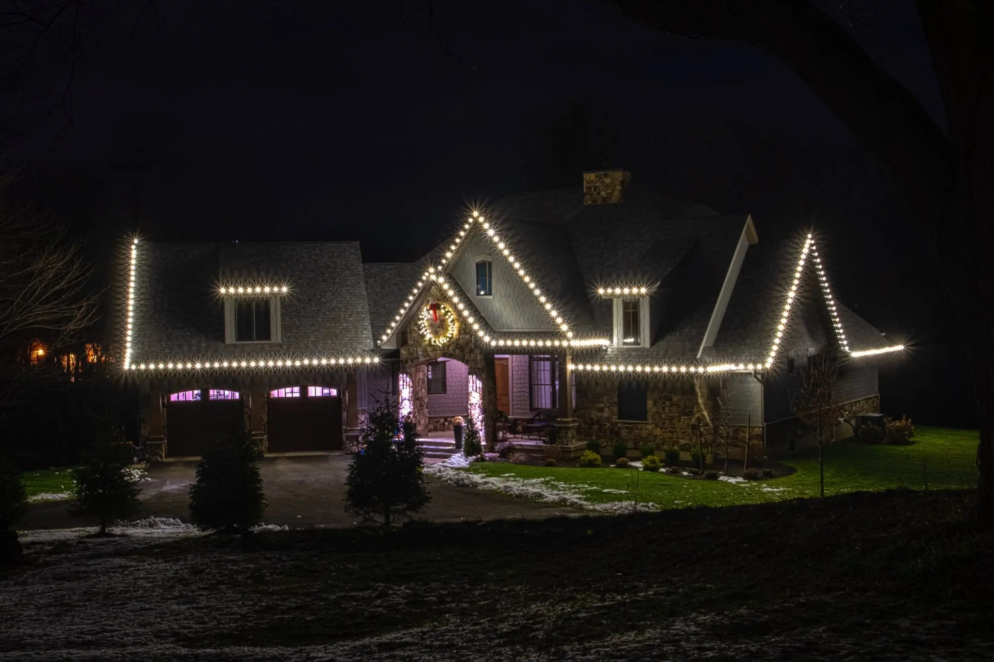 Home in Wynantskill professionally decorated for Christmas with white roof lights and a large live wreath above the entryway