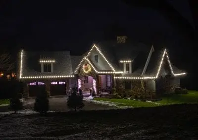 Home in Wynantskill professionally decorated for Christmas with white roof lights and a large live wreath above the entryway