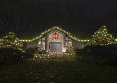 Single story home in Menands NY decorated for Christmas with white lights on the roof and trees with a live wreath hanging.
