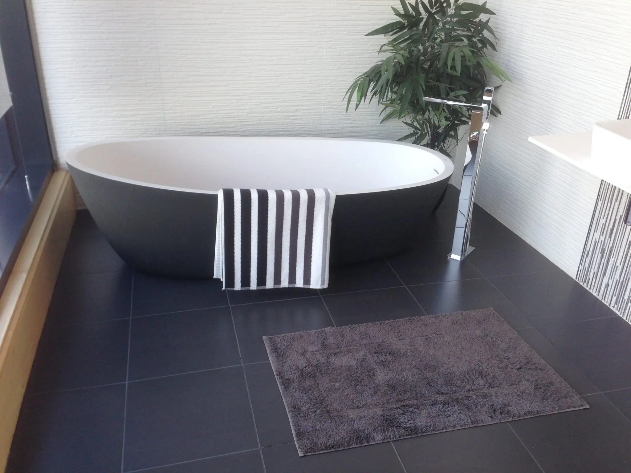 Bright bathroom with a striped towel, bathmat, and green plant
