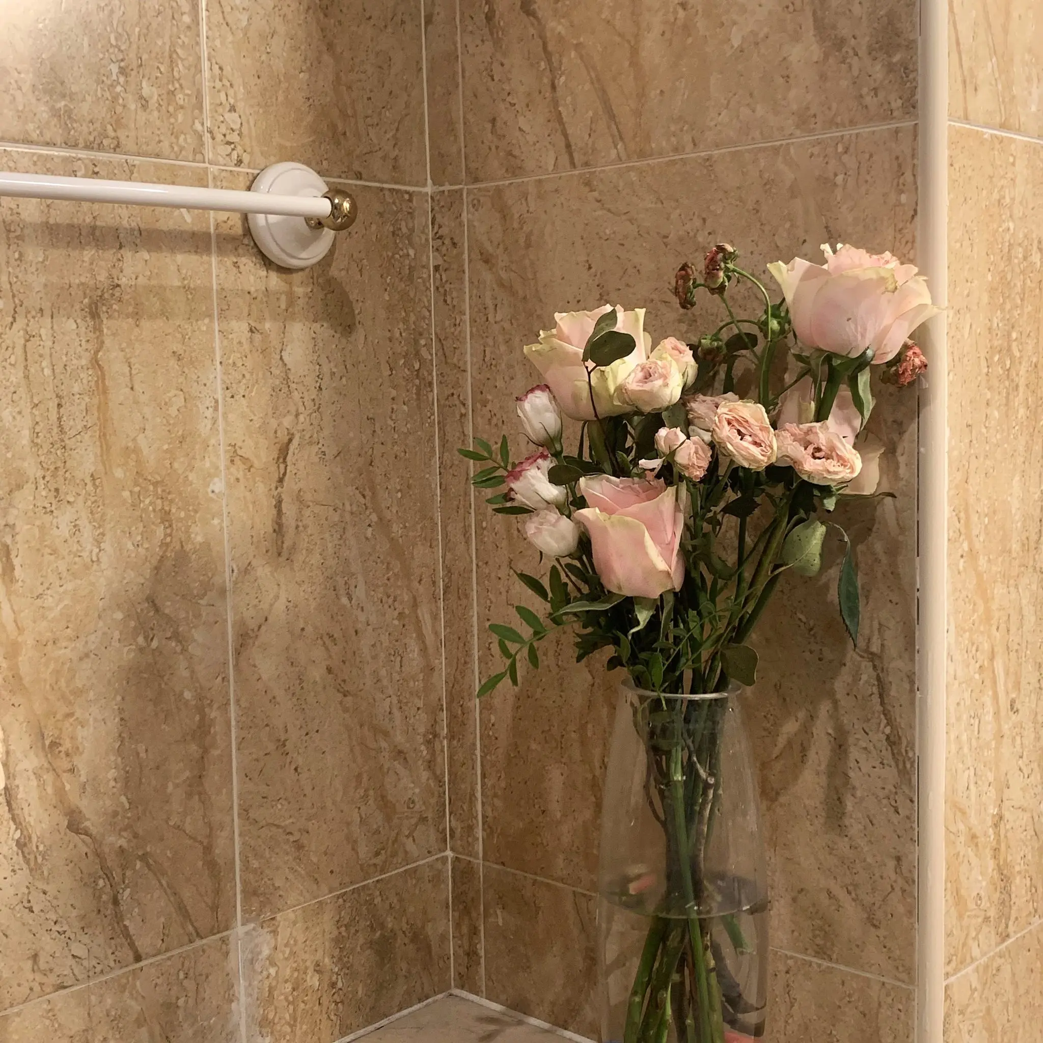 Pink roses beside an empty towel rail in a warm tiled bathroom