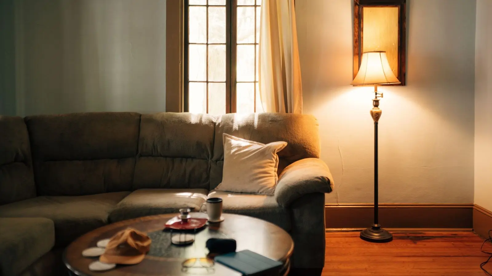 A warmly lit living room with a sofa, cushions, floor lamp, and round coffee table
