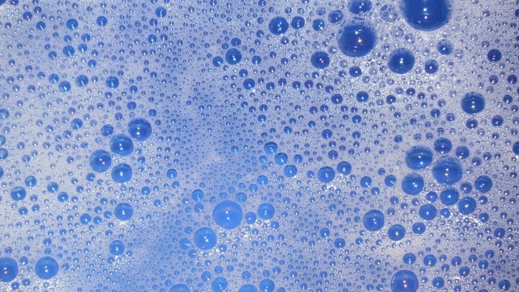 Close-up photograph of pale foam and clear bubbles over a blue background