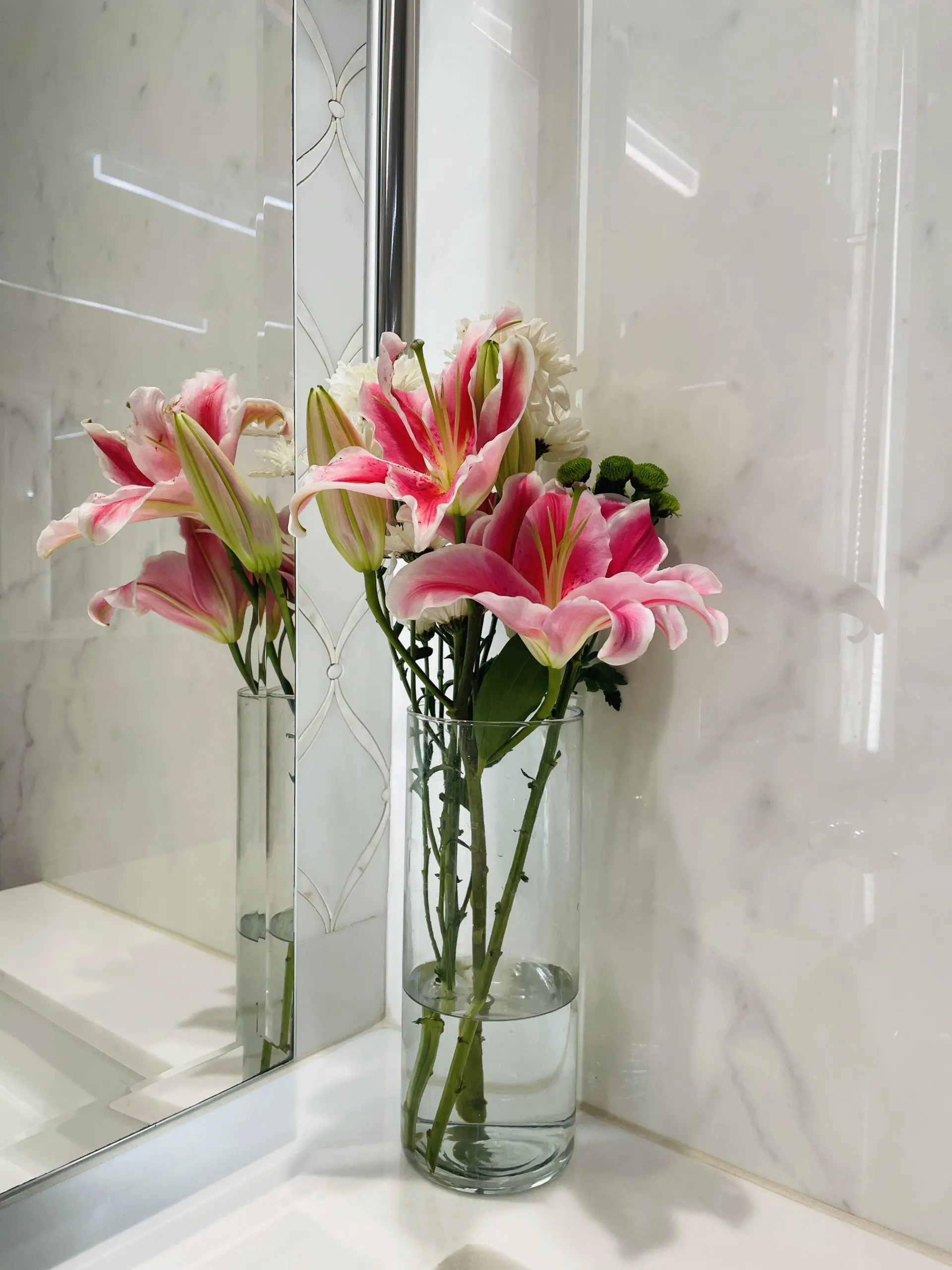 Pink lilies in a clear glass vase on a bathroom counter beside a mirror