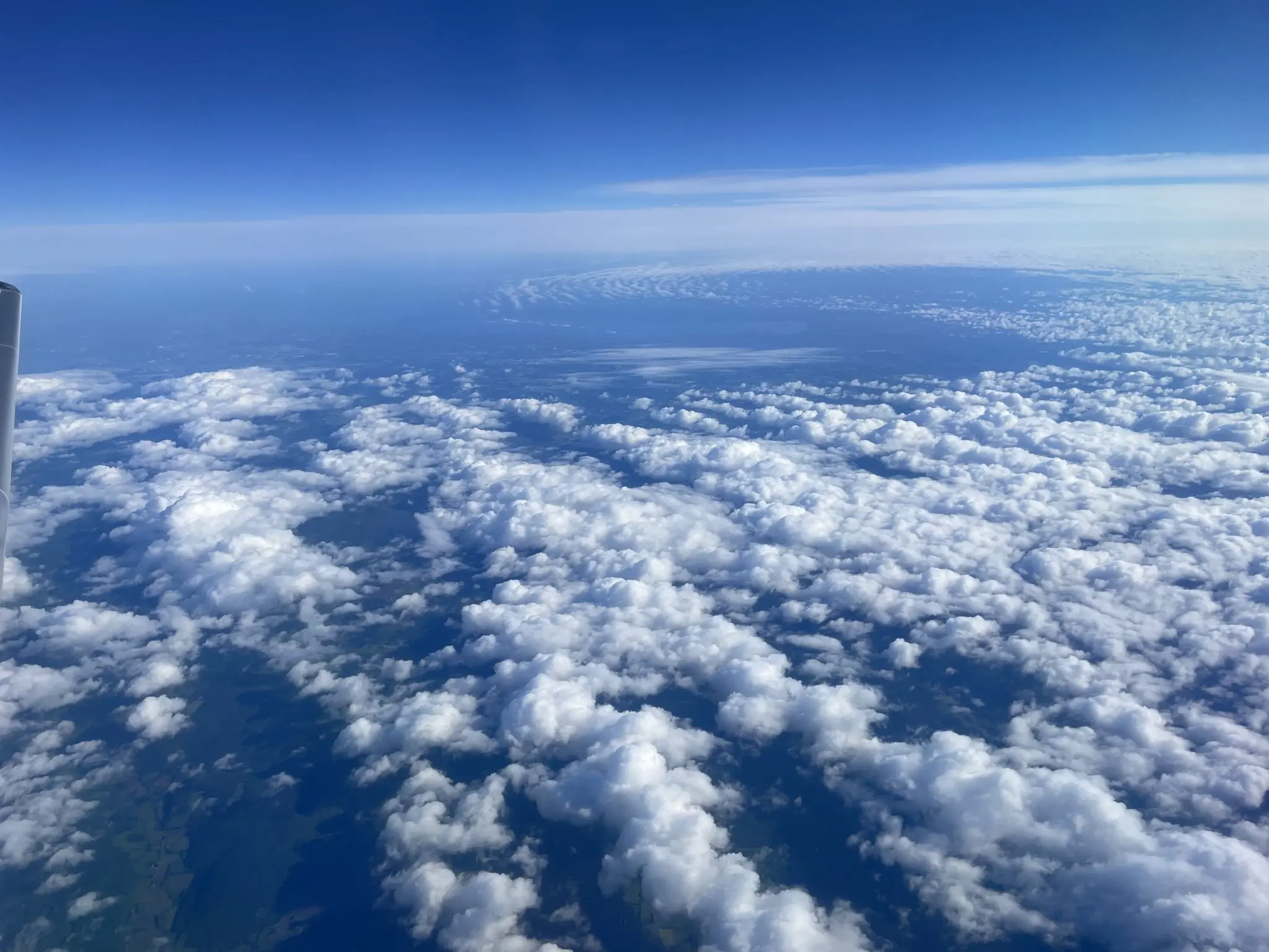 Clouds beneath a blue sky photographed from an airplane window