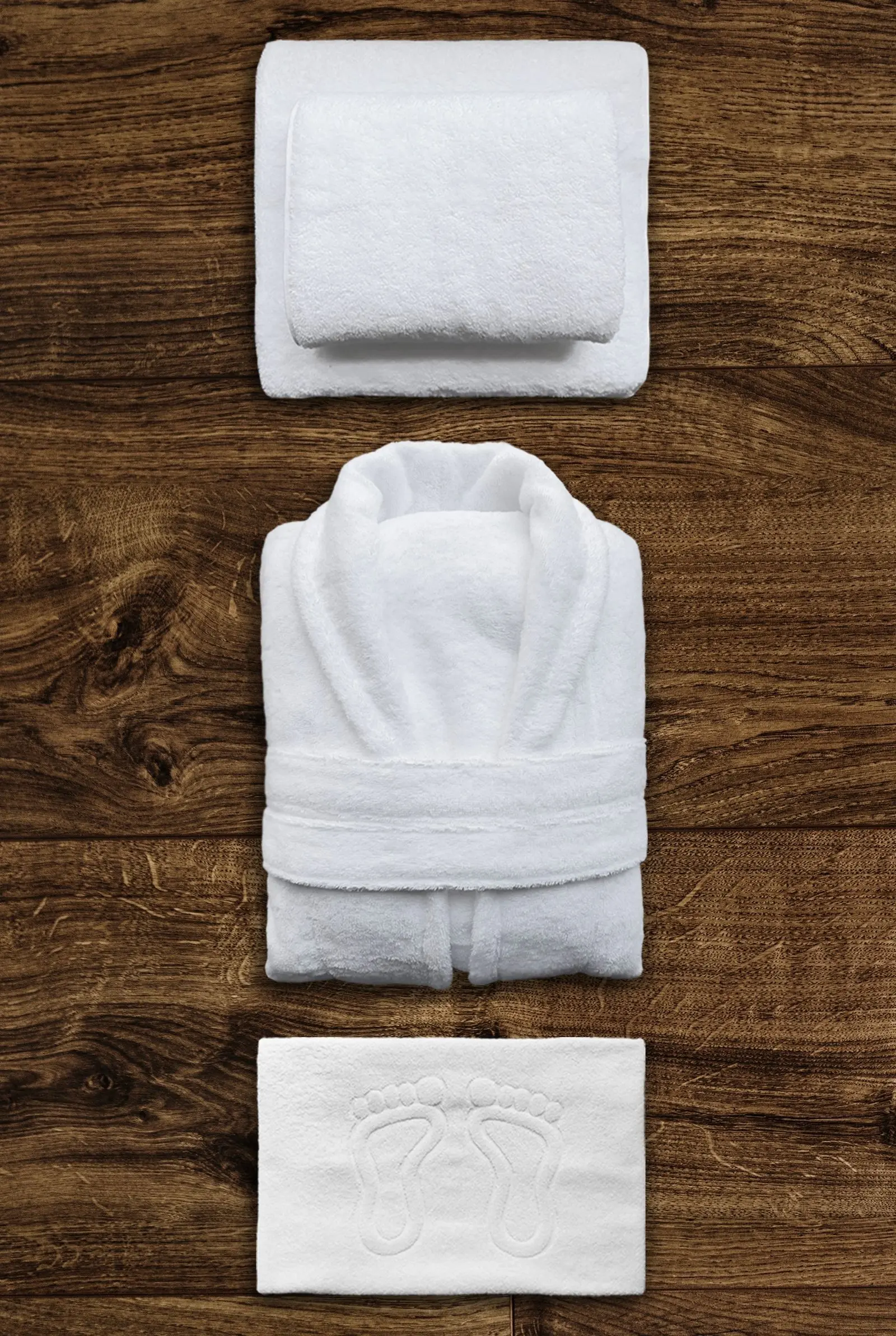 A folded white bathrobe, towels, and bath mat arranged on a wooden surface