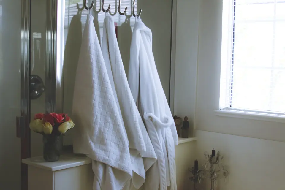 White bathroom linens and a robe hanging beside a bright window