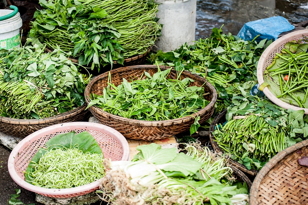 Fresh herbs and summer greens arranged in woven baskets at an outdoor market