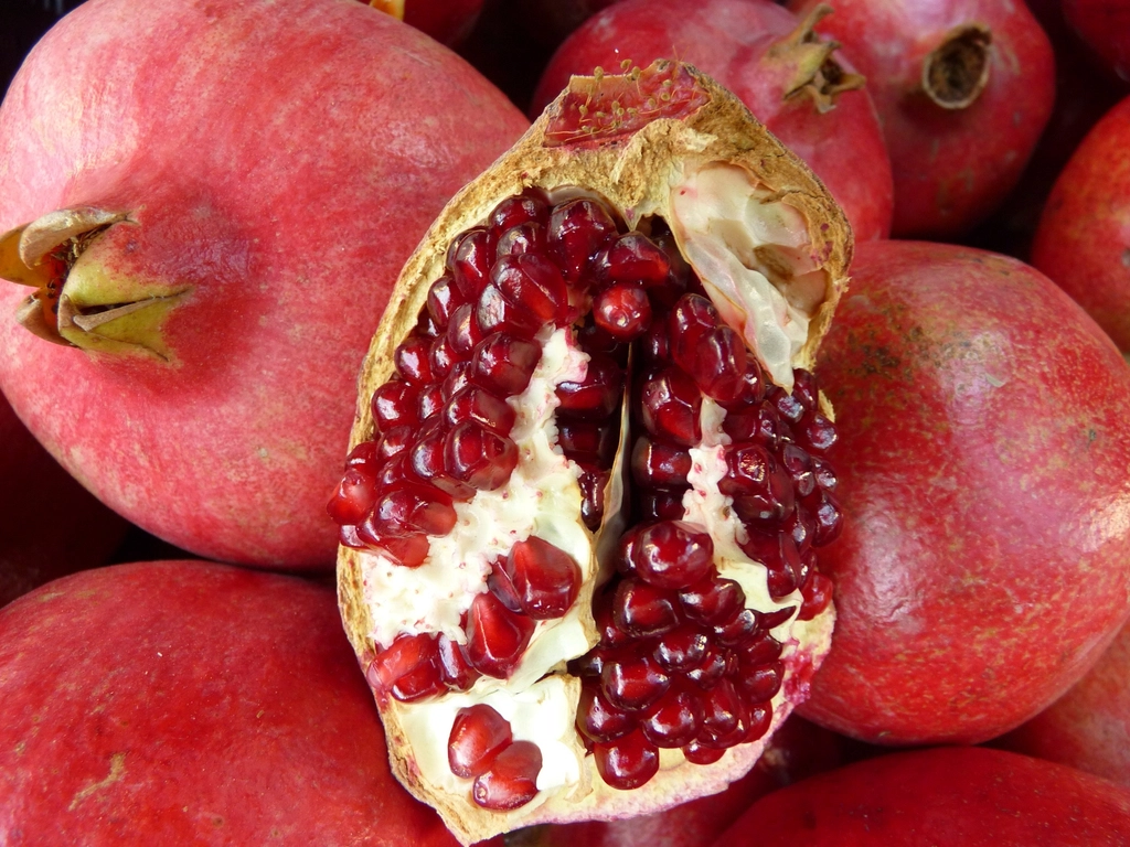 Whole pomegranates with an opened fruit showing ruby-red seeds