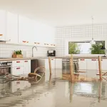 Flooded kitchen with water covering the floor, overturned chairs, and modern white cabinetry.