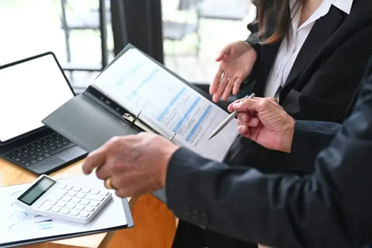Two professionals discuss documents while a laptop and calculator are on the table.