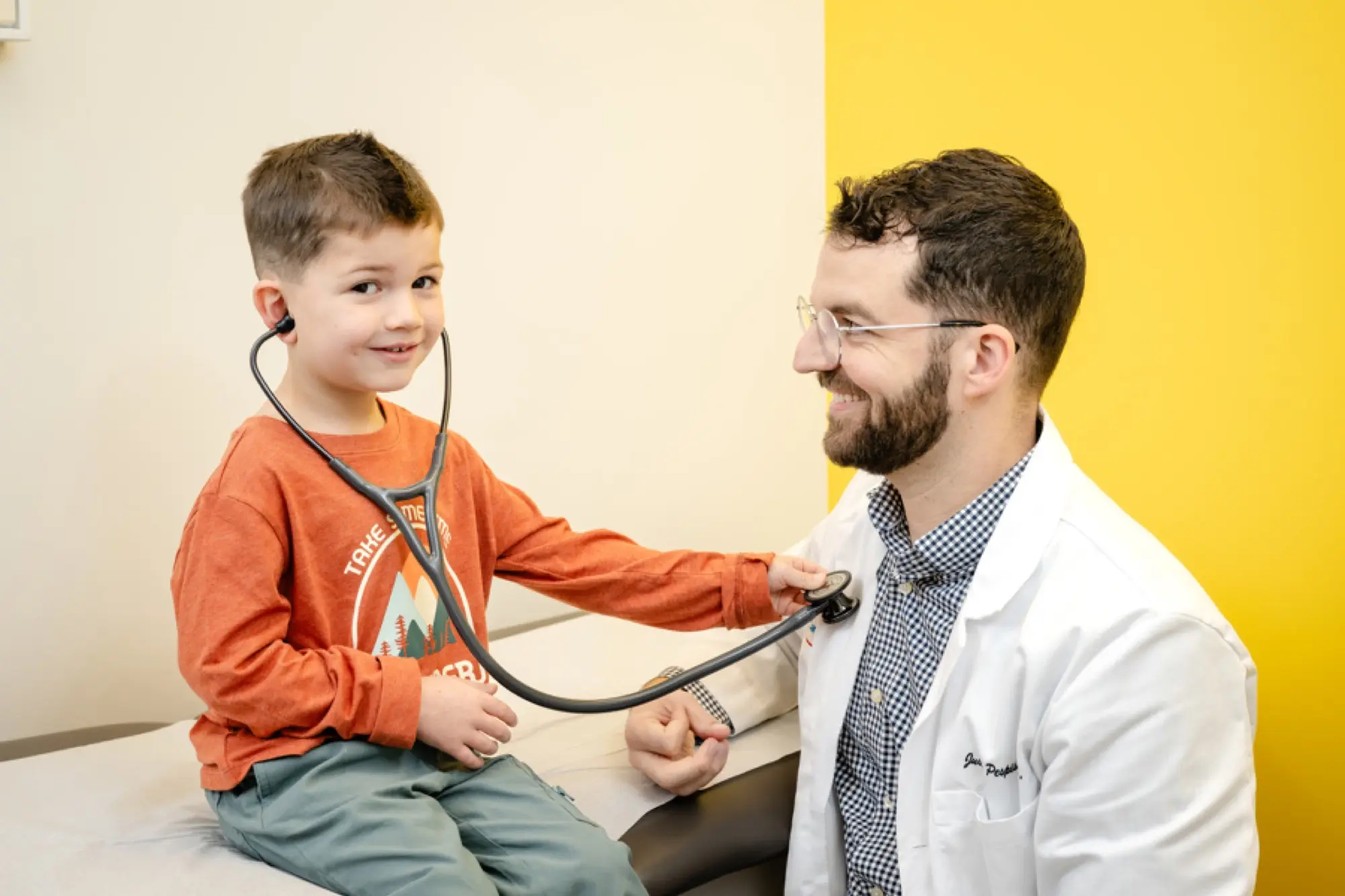 Dr. Justin Pespisa letting a smiling boy listen to his heartbeat through a stethoscope