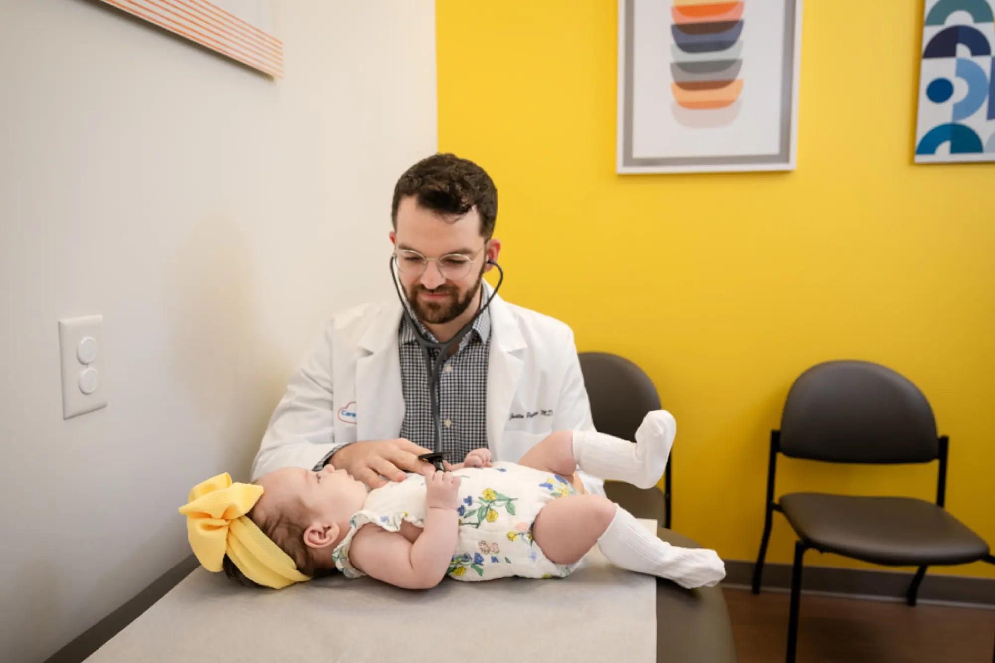 Dr. Justin Pespisa gently examining a smiling baby on the exam table