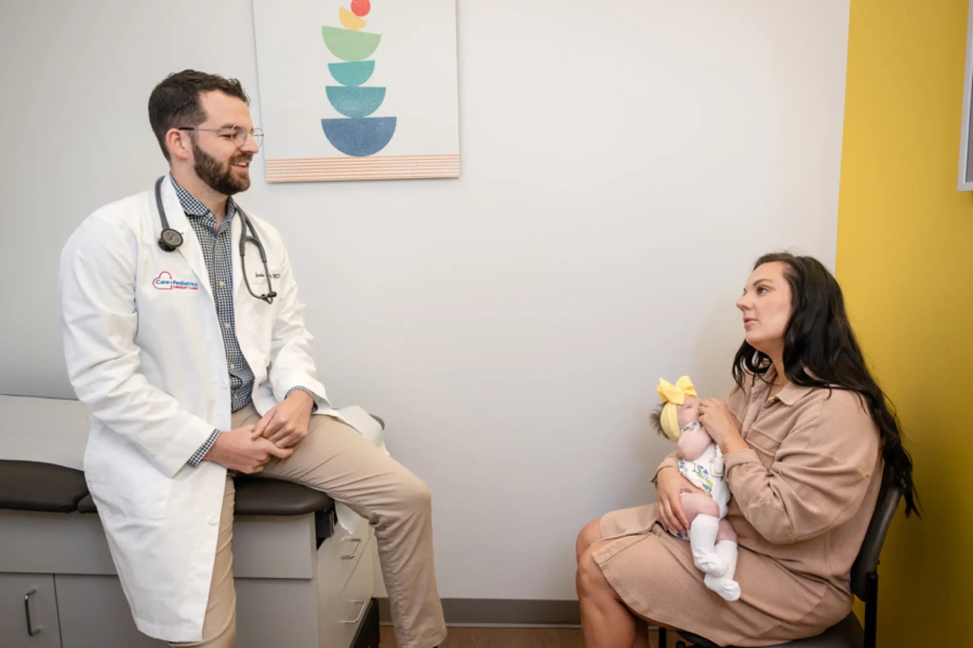 A Care+ physician chatting with a mother holding her newborn in a South OKC exam room