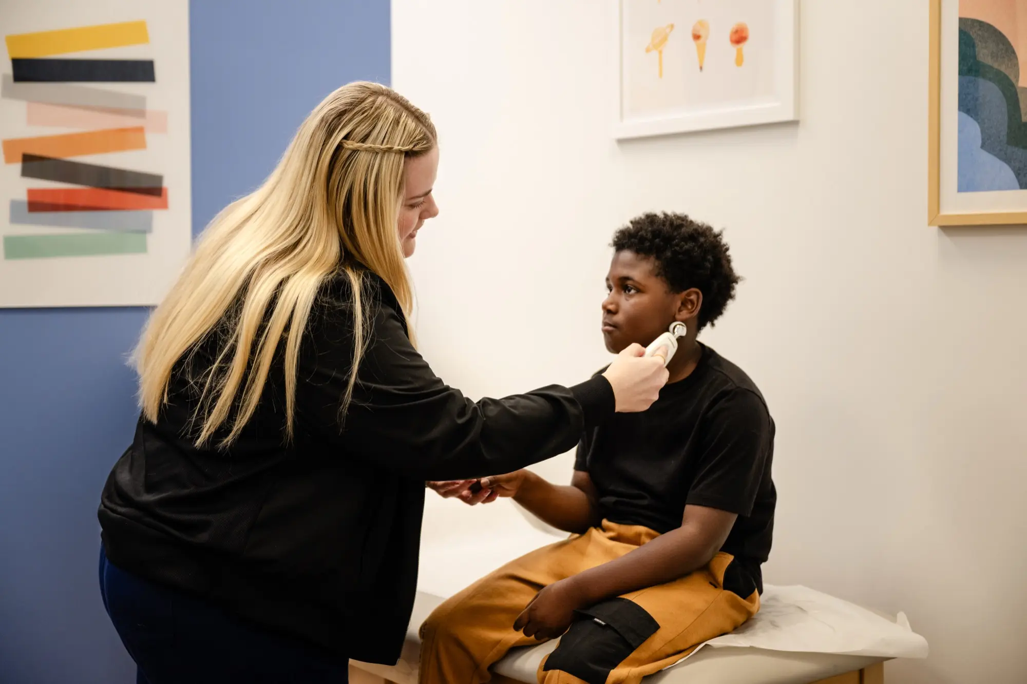 A Care+ provider gently checking a young boy's ear during a calm exam-room visit