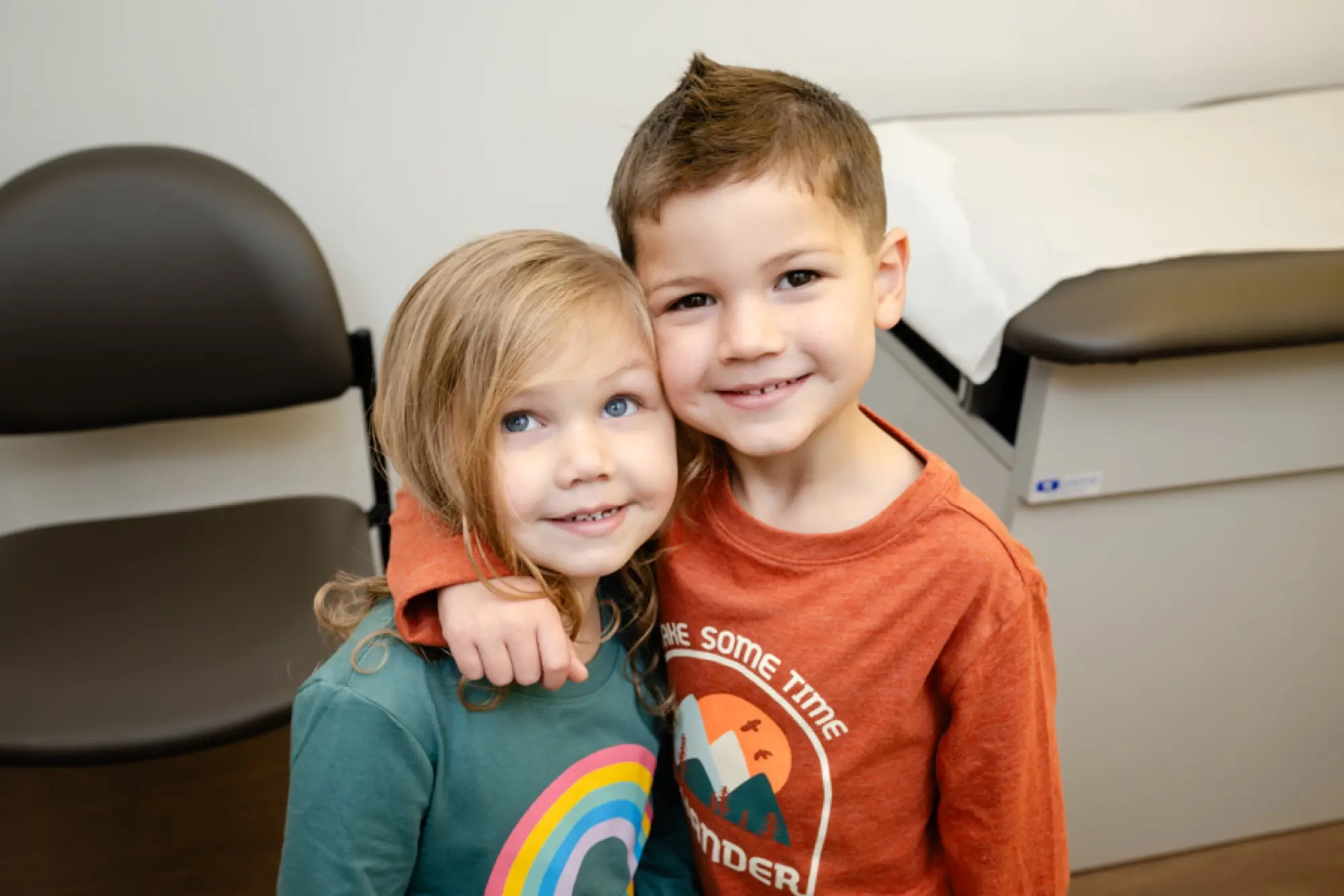A big brother hugging his little sister in the exam room at Care+ Pediatrics