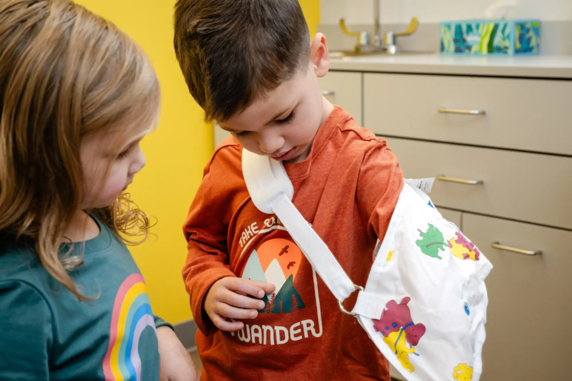 A young boy checking out his new arm sling after injury care while his sister looks on