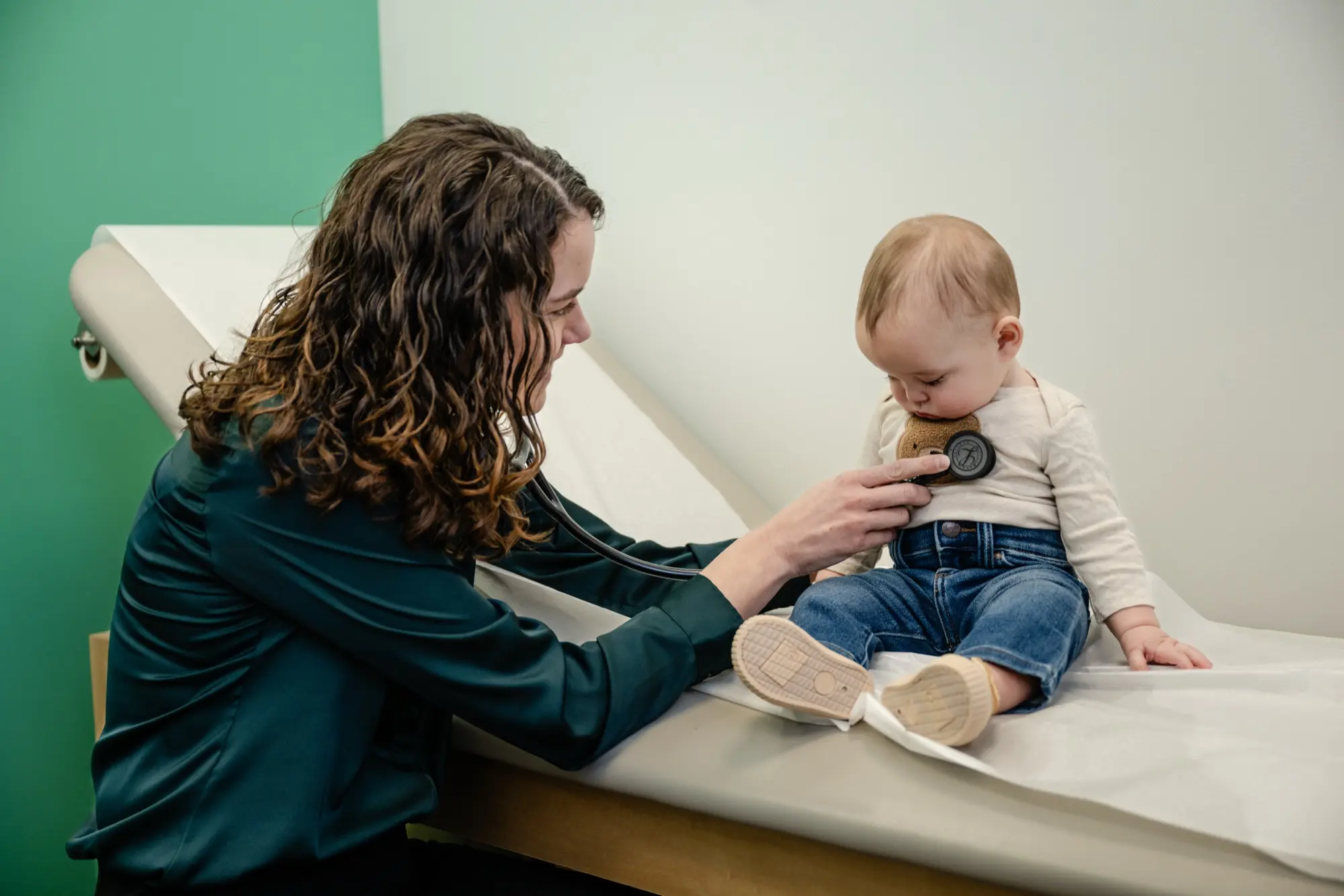 A Care+ provider listening to a baby's chest with a stethoscope during an exam
