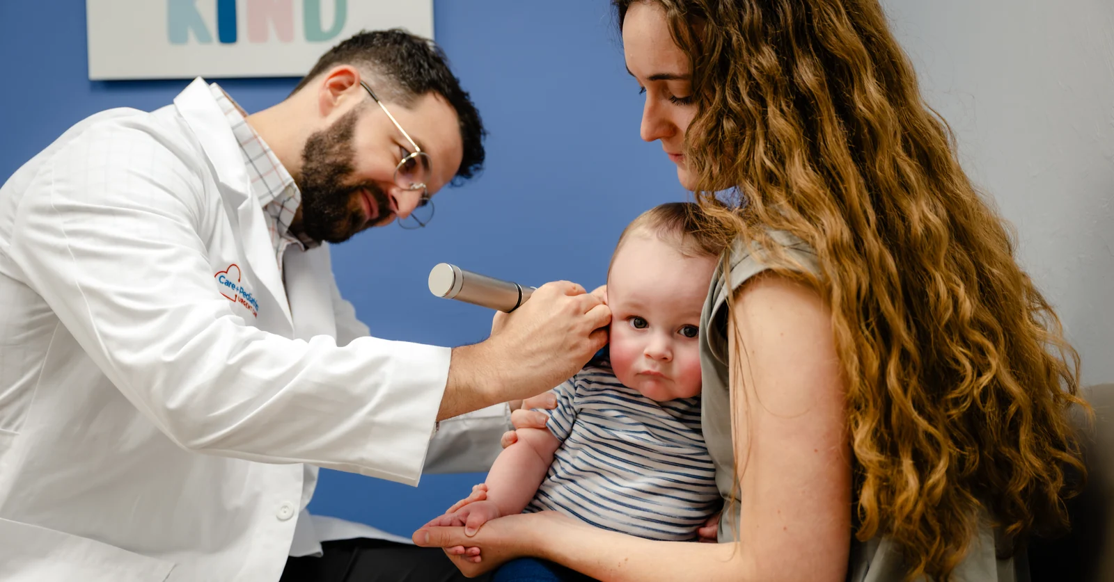 A Care+ Pediatrics provider examining a baby’s ear while the child sits in a parent’s lap