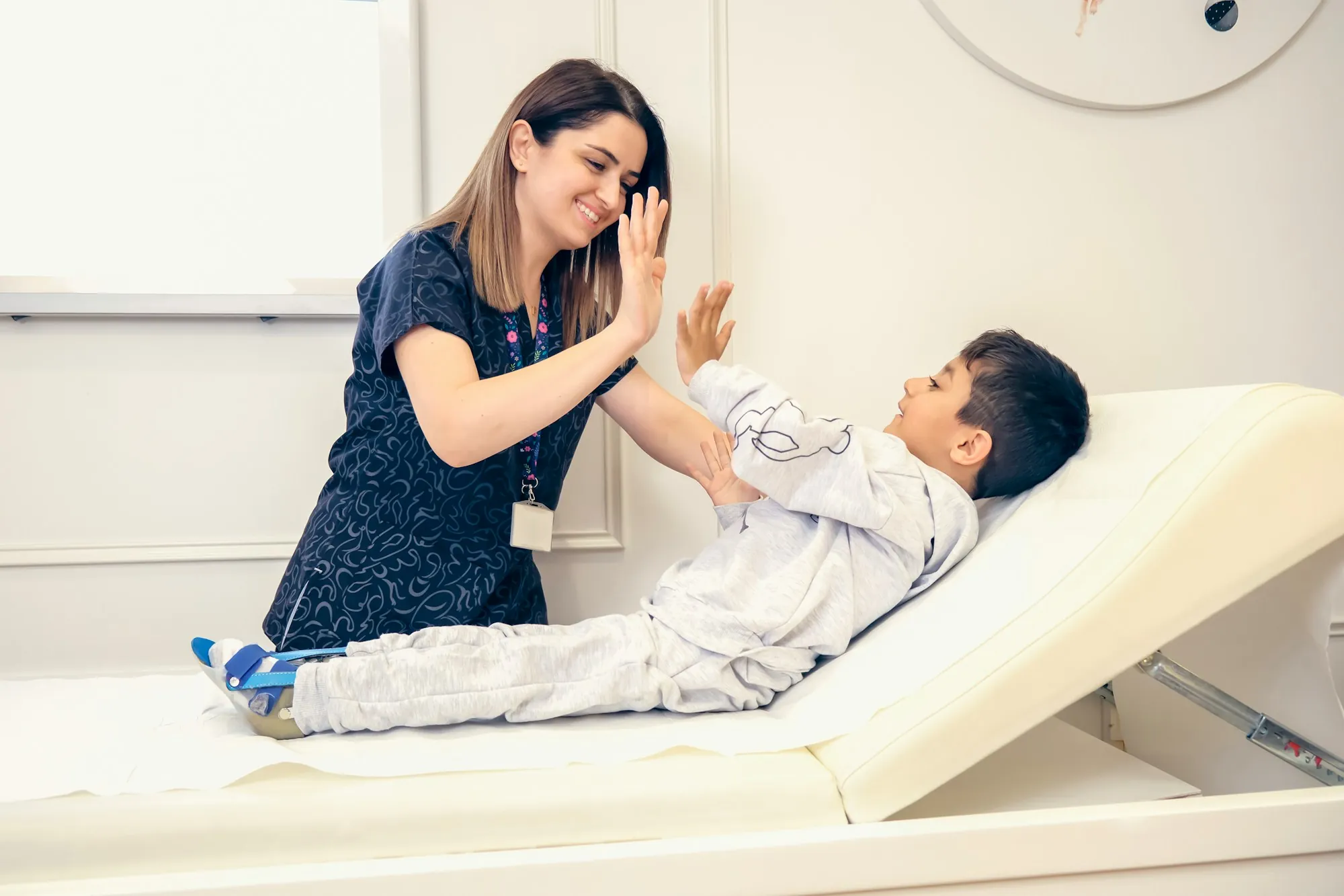 A smiling pediatric provider high-fiving a young boy on the exam table