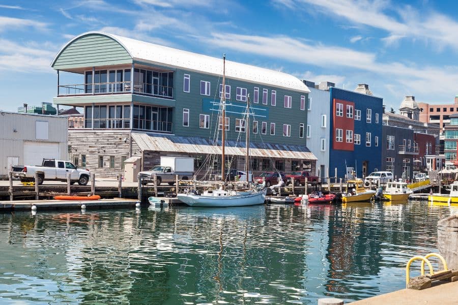 Colorful waterfront buildings along a harbor with boats and calm water reflecting the sky.