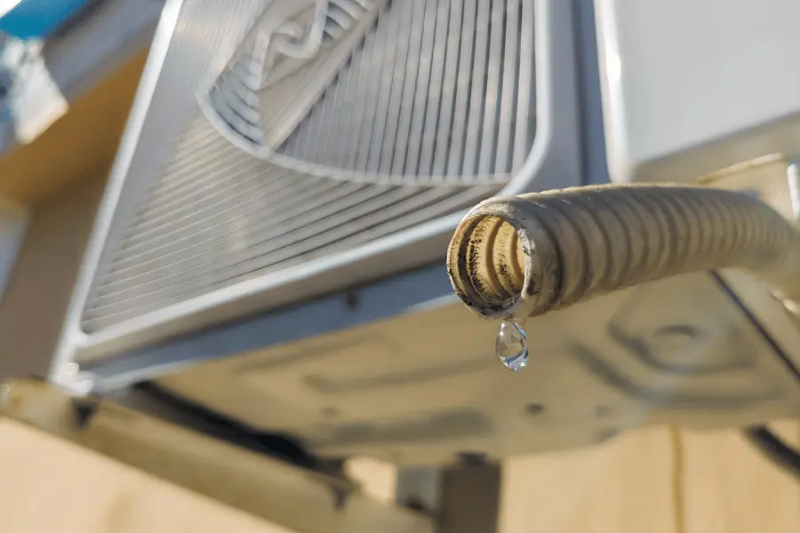 Outdoor air conditioning unit with a flexible drain hose dripping a water droplet, indicating condensate discharge on a sunny day.