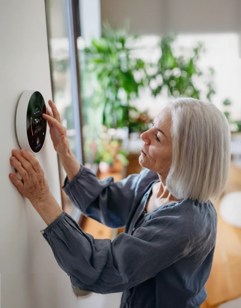 Senior woman adjusting a smart thermostat on a wall in a bright, plant-filled room.