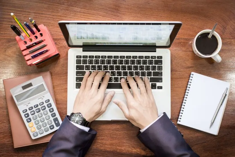 Hands typing on laptop with financial tools and notebook for accounting and financial management services.