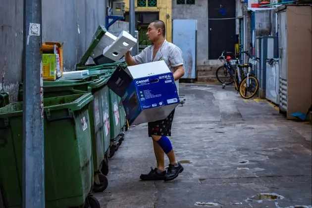 Man throwing cardboard boxes into green alleyway commercial dumpsters
