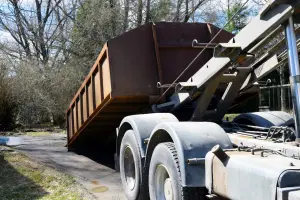 Roll-off dumpster truck delivering a large brown metal bin