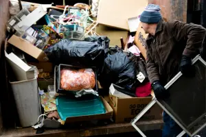 Man loading household trash and boxes into a dumpster rental