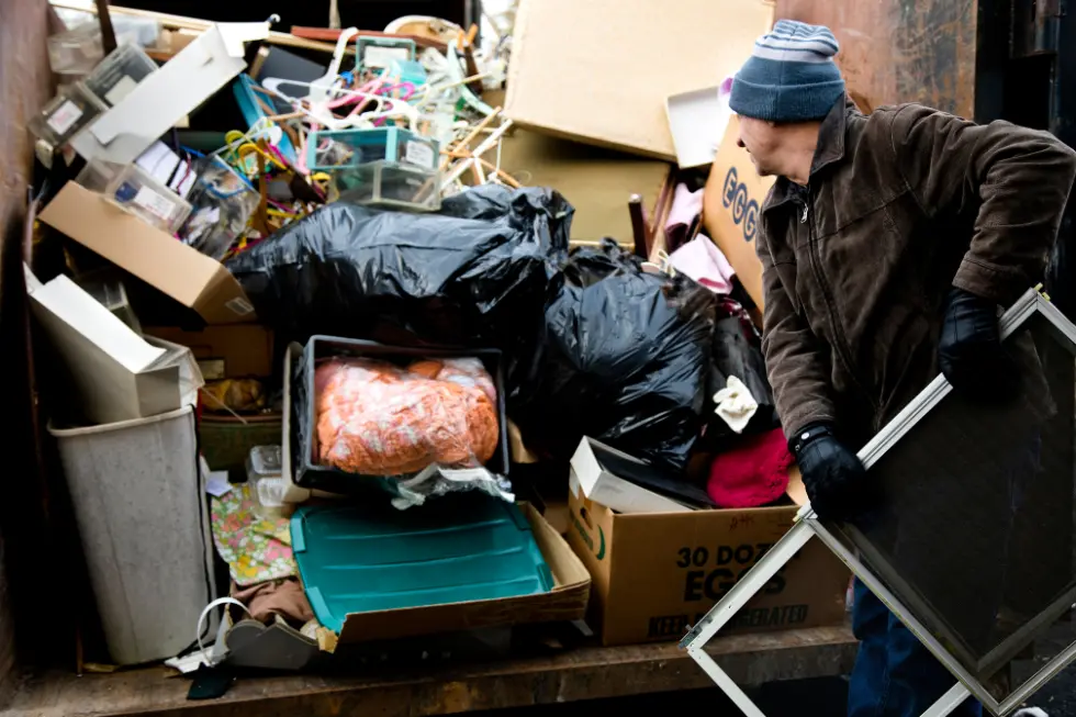Man loading household trash and boxes into a dumpster rental