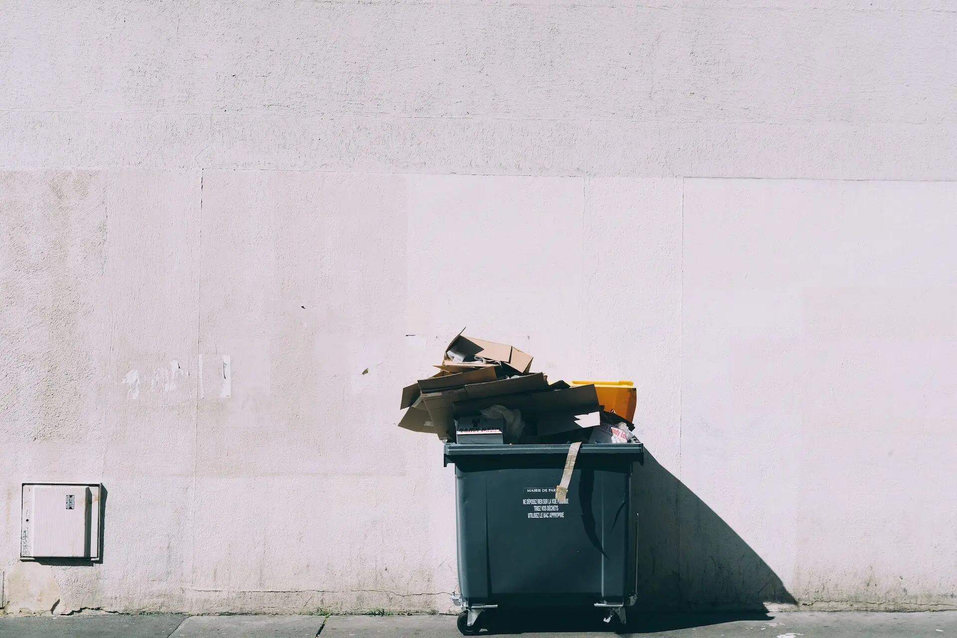 Commercial trash bin overflowing with cardboard boxes against a wall