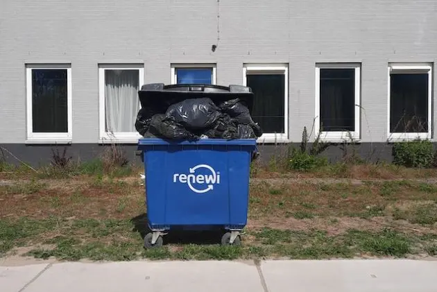 Blue Renewi commercial dumpster overflowing with black trash bags outdoors