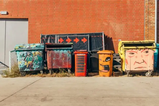 Colorful graffiti painted small dumpsters lined up near brick wall