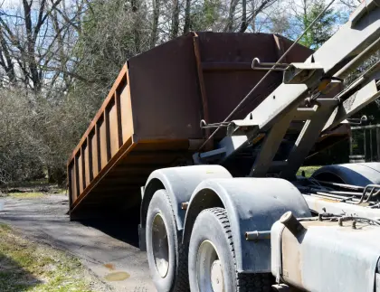 Roll-off dumpster truck delivering a large brown metal bin