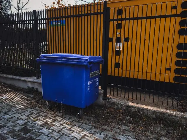 Blue commercial dumpster rental parked outside a fenced utility enclosure