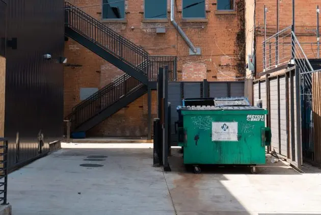 Green commercial recycling dumpster rental in an alleyway enclosure