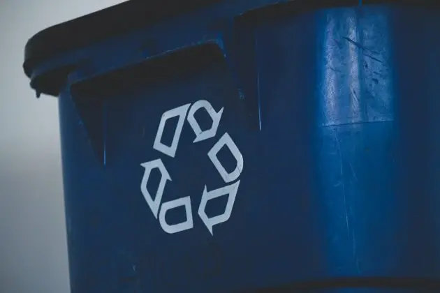 White recycling symbol on side of blue plastic dumpster bin