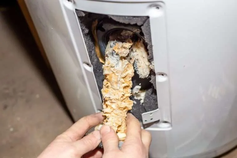 Repair and maintenance of boilers. The master plumber pulls out a tubular electric heater covered with lime scale from the hole in the boiler.