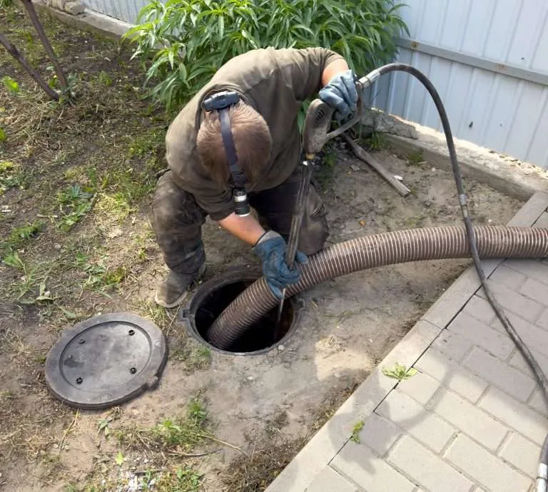 service worker using a heavy-duty suction hose and high-pressure tool to clean and pump out an underground septic tank