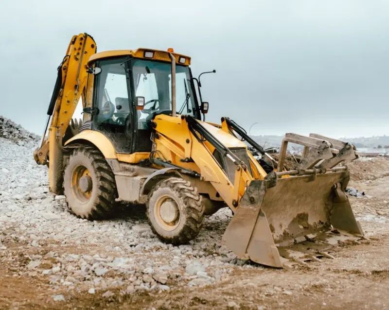 yellow backhoe loader parked on a gravel construction site
