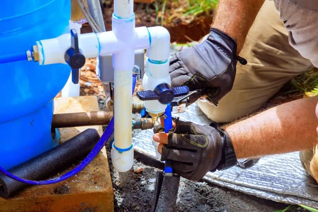 Skilled worker repairs artesian water well unit using tools and materials in a construction area.