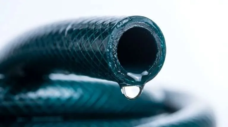 close-up view of the open end of a green textured garden hose with a single clear water droplet hanging from the edge